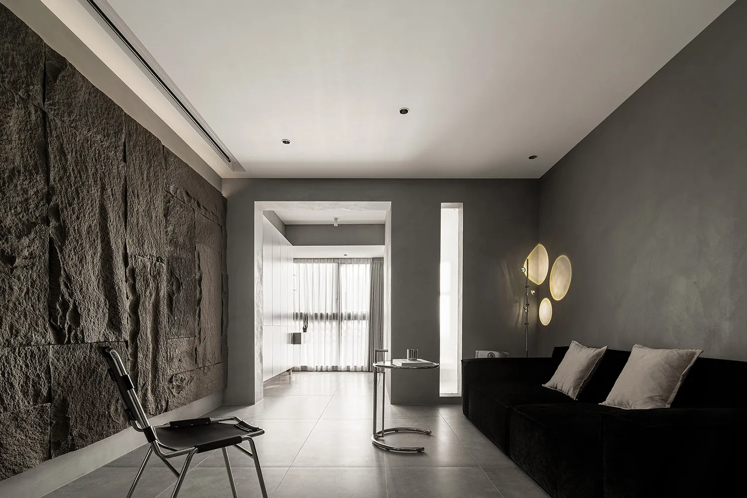 A minimalist residential interior featuring polished concrete walls, a black sofa, and modern lighting.