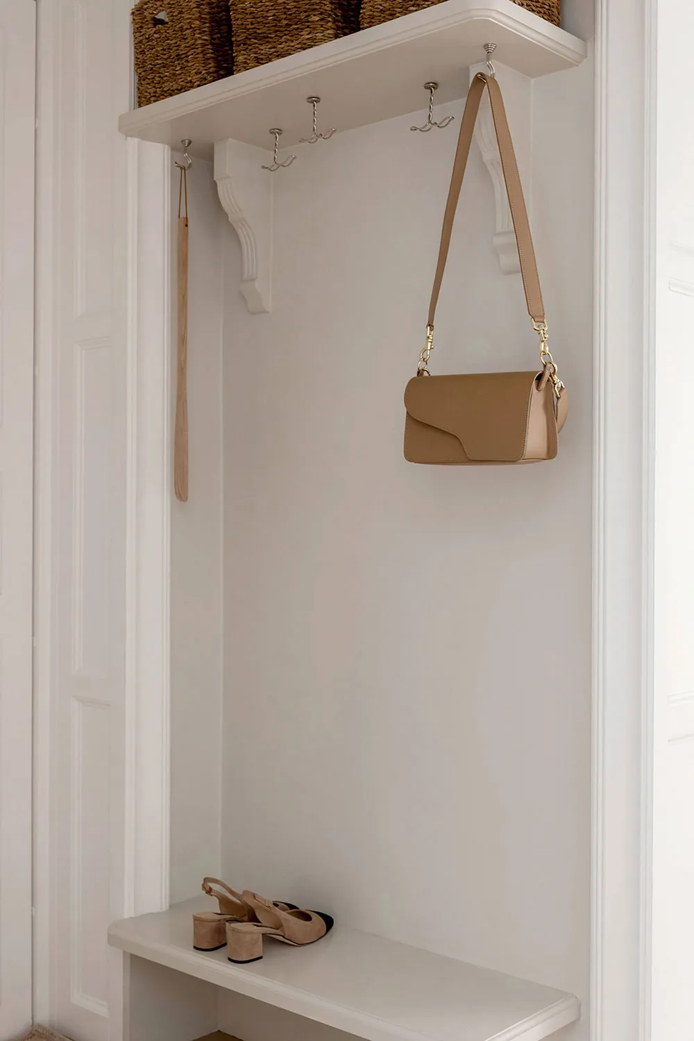 A minimalist white storage space with a bench, hooks, and a bag hanging.