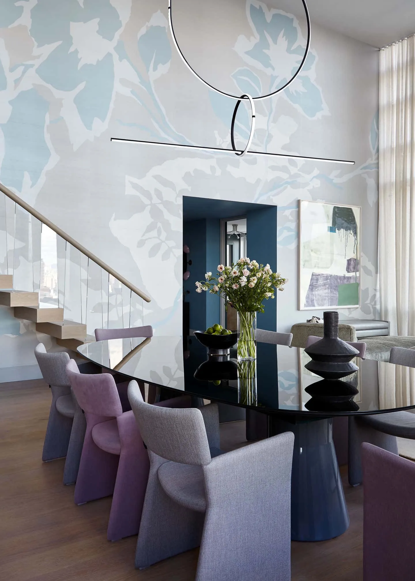A modern dining room with a glass table, purple and gray chairs, and abstract art on the wall.