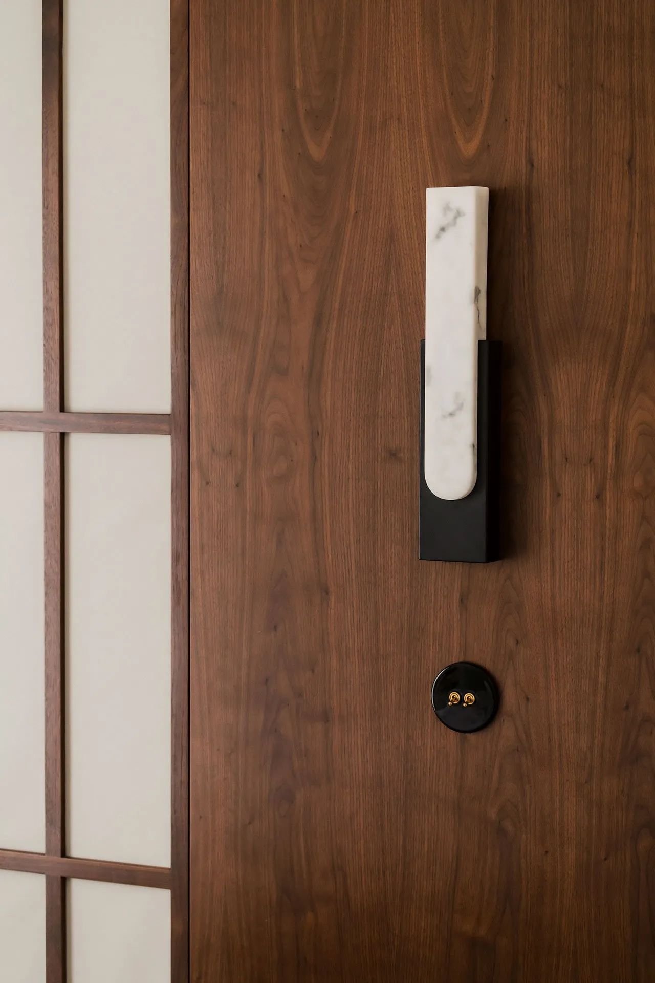 A modern entryway featuring a wooden door with a white marble handle and a black light switch.
