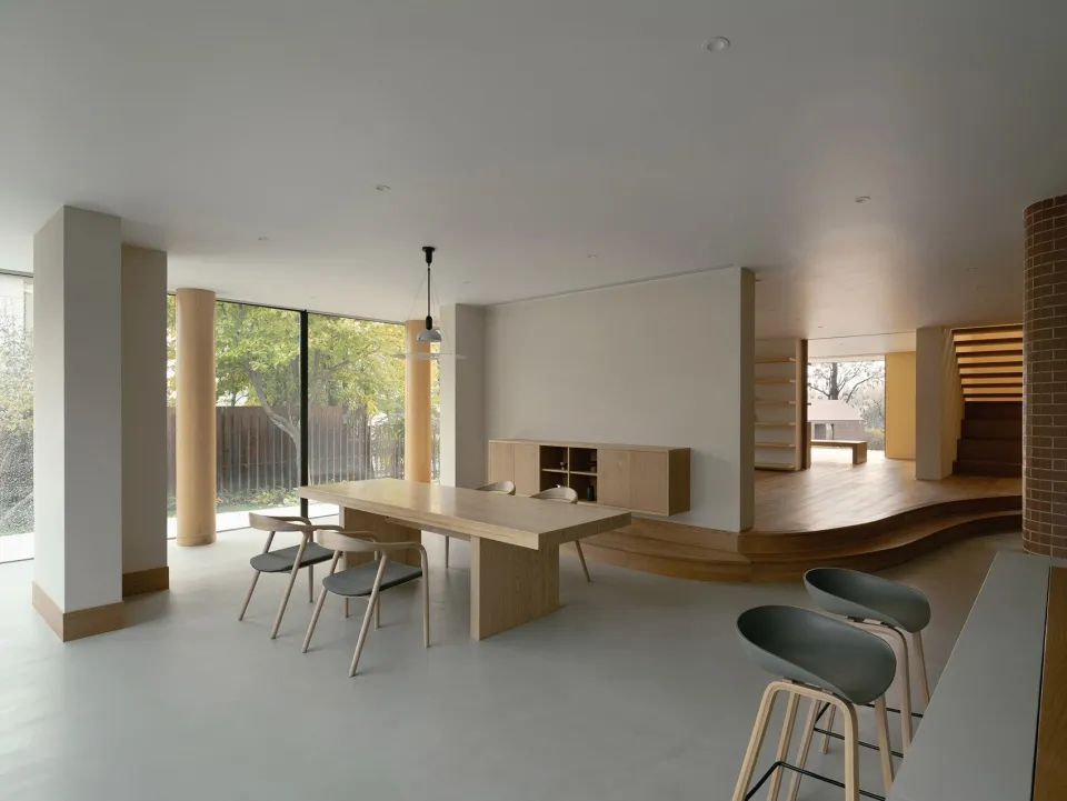 A modern living room with a wooden dining table and chairs next to a kitchen area with a bar in a contemporary home design.
