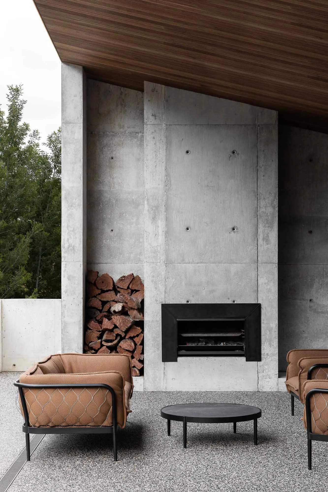 A modern living space with a concrete wall, a black fireplace insert, and brown upholstered armchairs.
