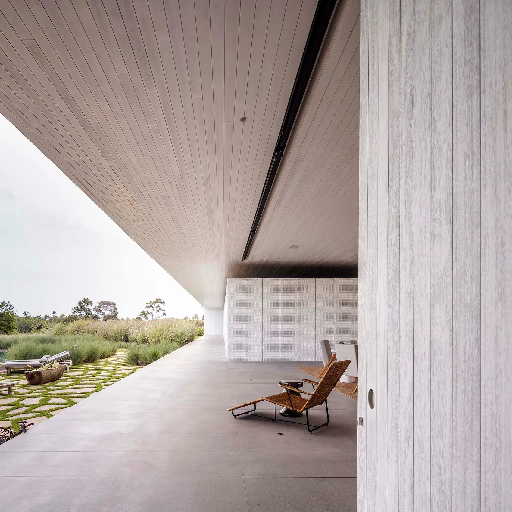 An image of a minimalist, modern residential outdoor space with a concrete floor and walls, featuring a single natural woven 