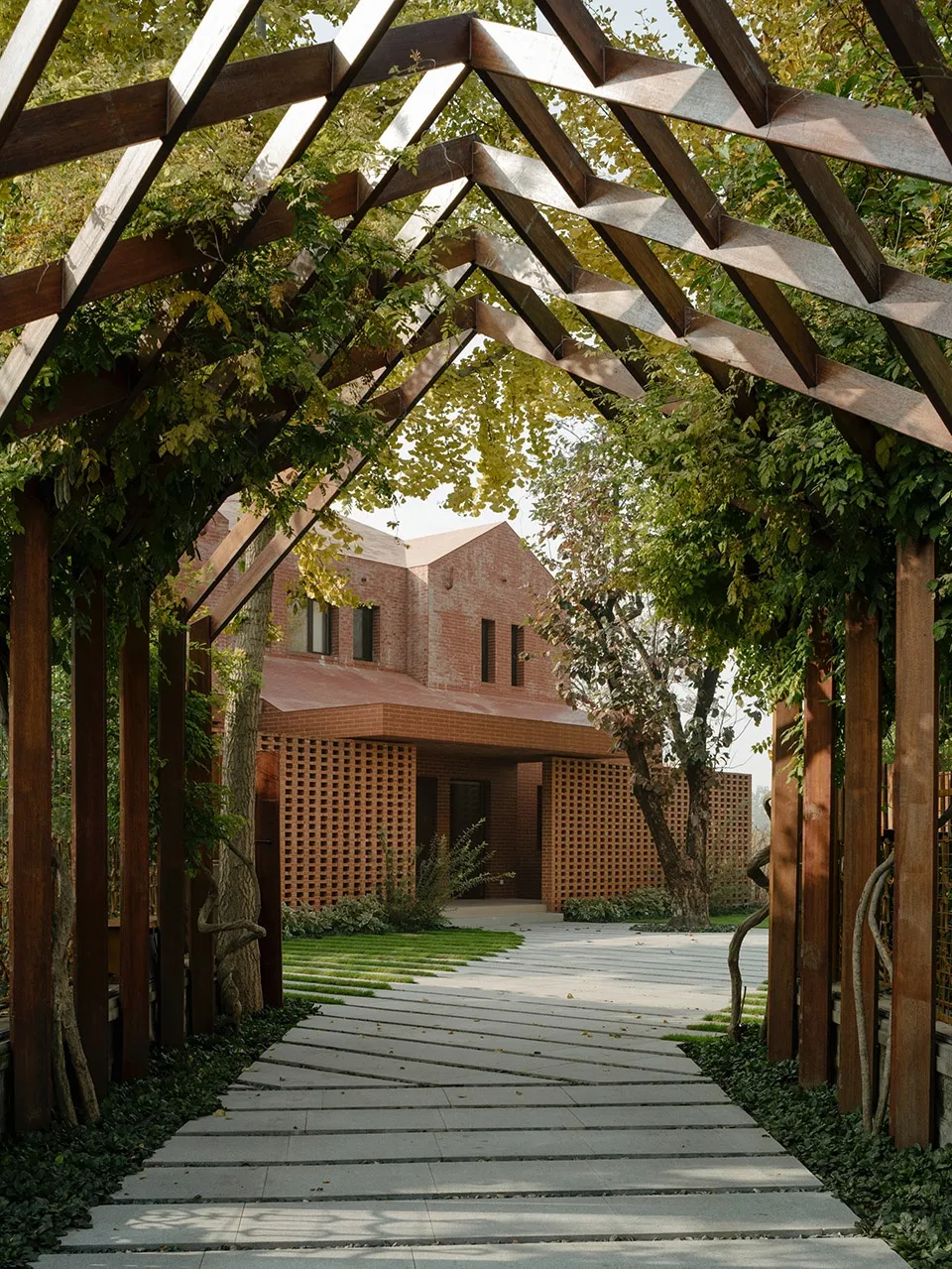 A pathway leading to a wooden pavilion surrounded by greenery, with a wooden pergola overhead.