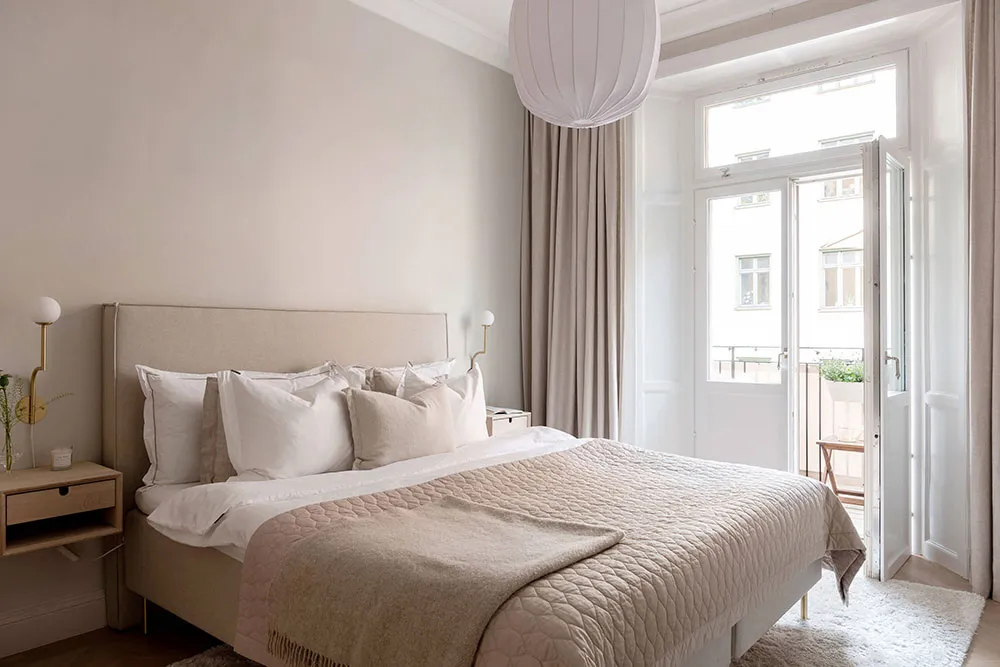 A minimalist bedroom featuring a bed with fabric bedding and wooden furniture, natural light streaming through the window.