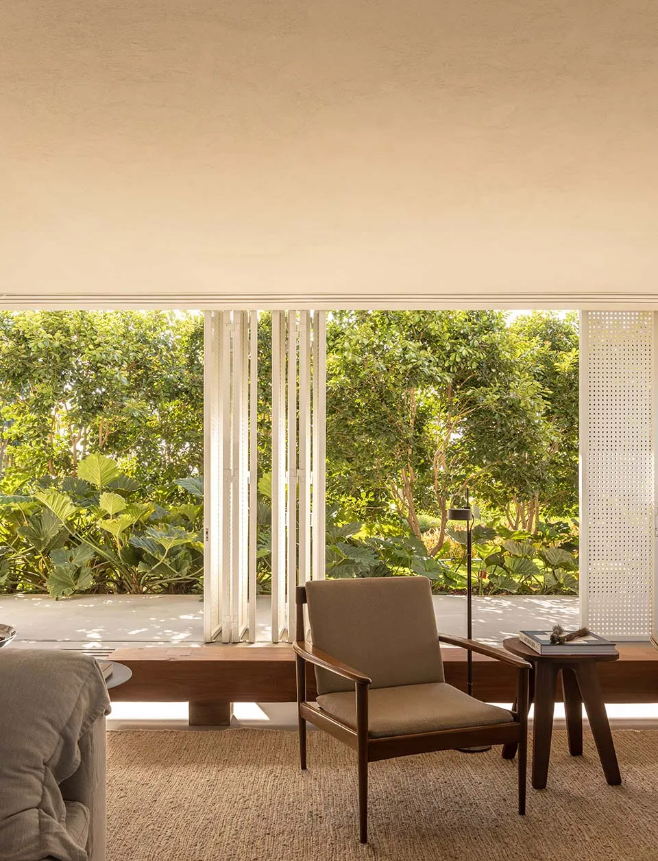 A minimalist living room with natural light, featuring a wooden chair and side table against a wall of windows.