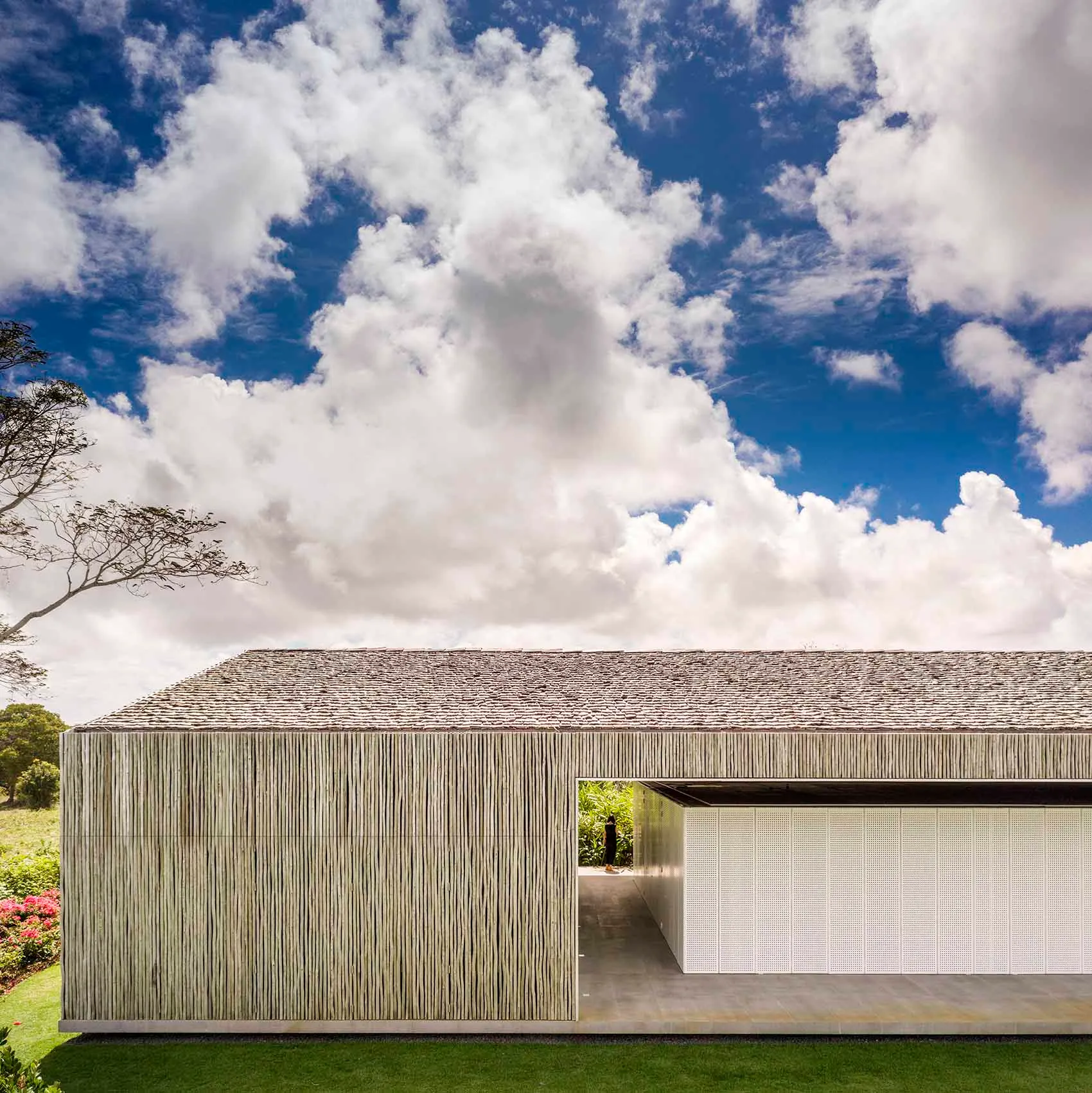 A modern house with a bamboo cladding exterior under a cloudy blue sky.