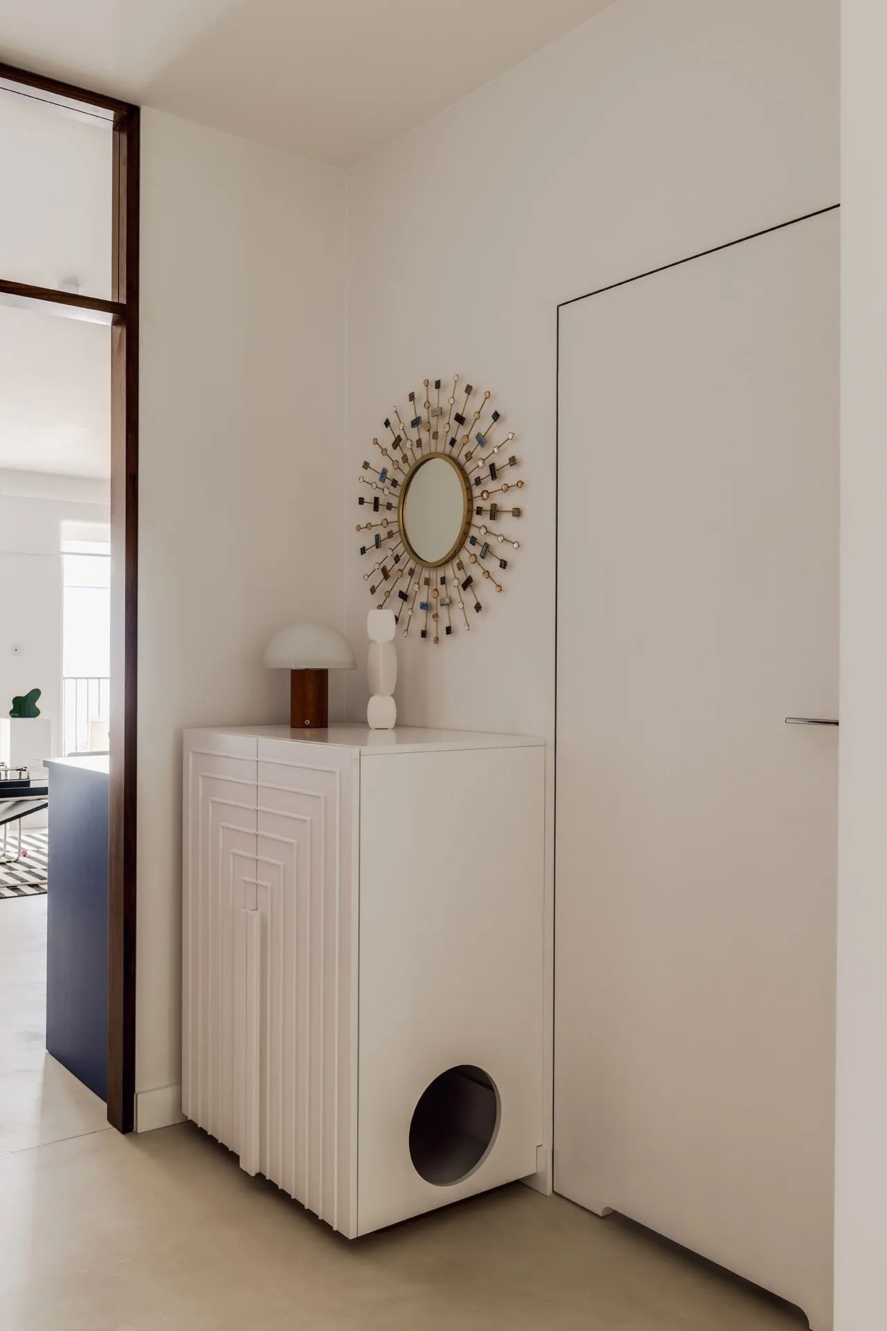A modern white entryway cabinet with a sunburst mirror and a simple lamp.