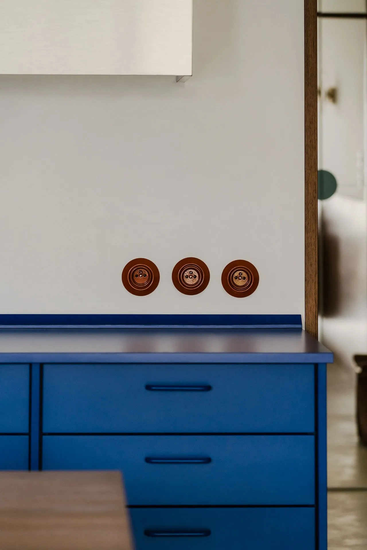 Close-up of a blue dresser with three brass light switches against a white background.