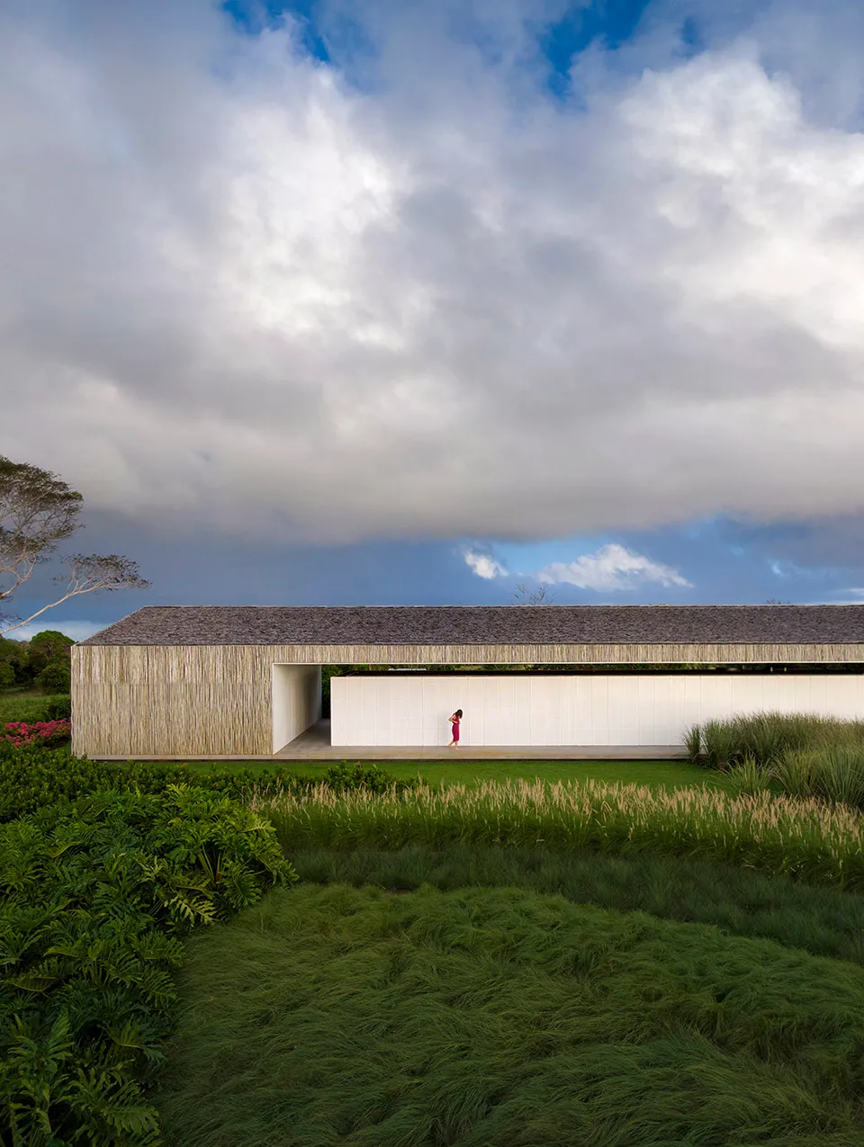 A modern house with green packgrass in the foreground and a cloudy sky above.