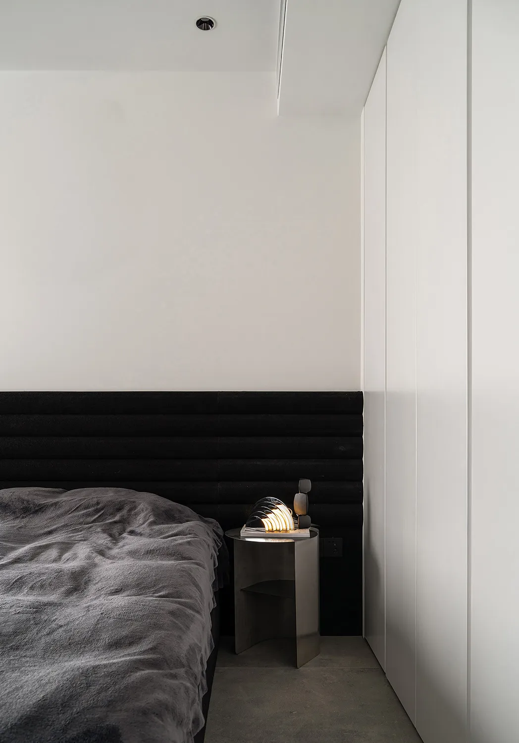 A modern minimalist bedroom featuring a black upholstered bed and a metallic bedside table with a modern lamp.