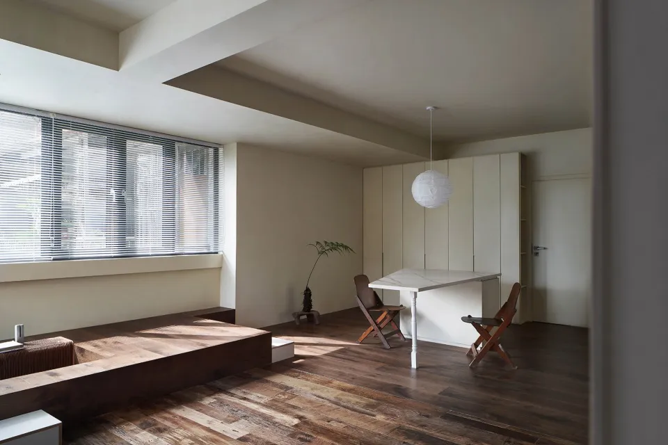 A minimalist living space featuring a wooden platform, marble table, and mixed-use furniture.