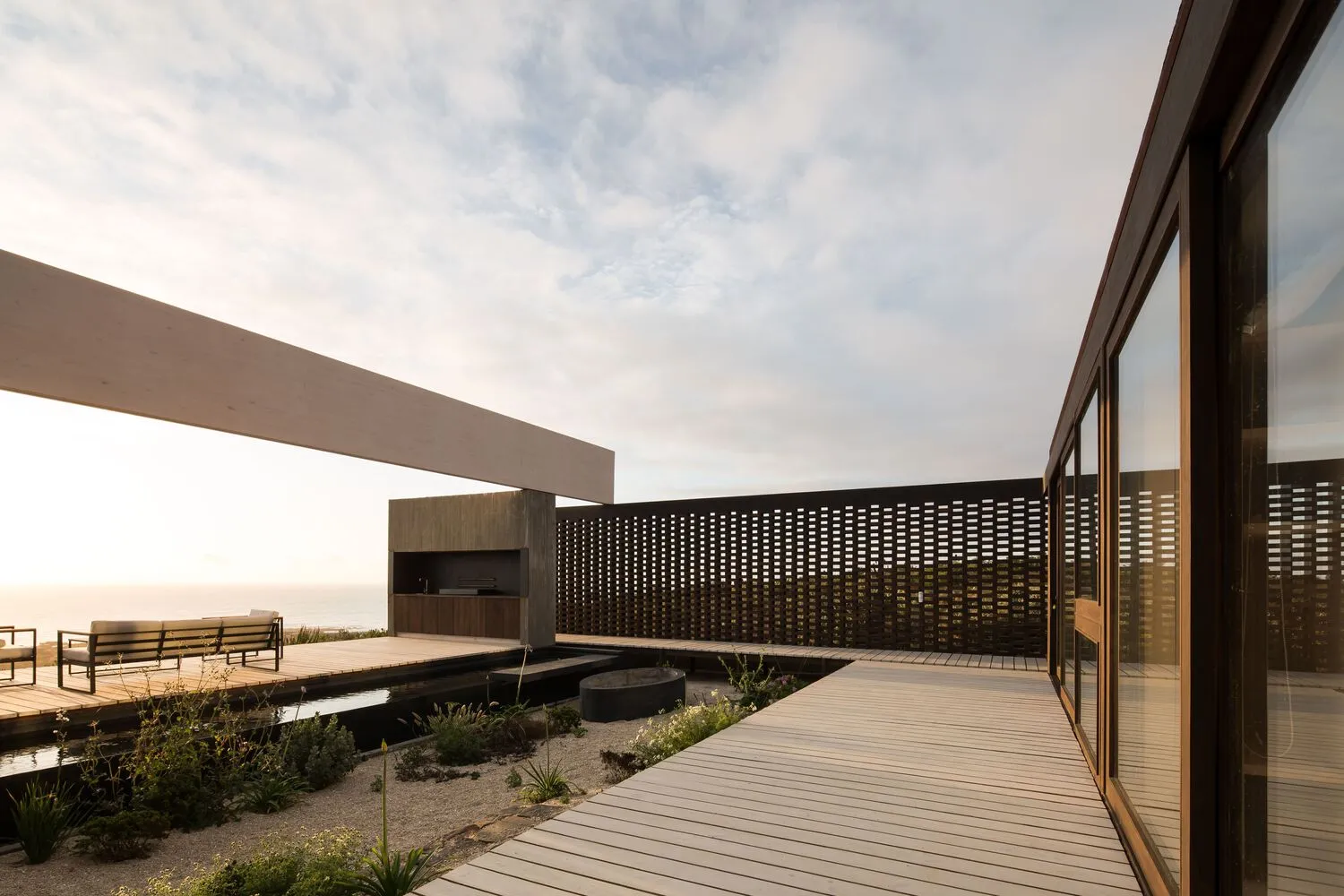 Modern residential exterior featuring a wooden deck, metal fencing, and glass walls.
