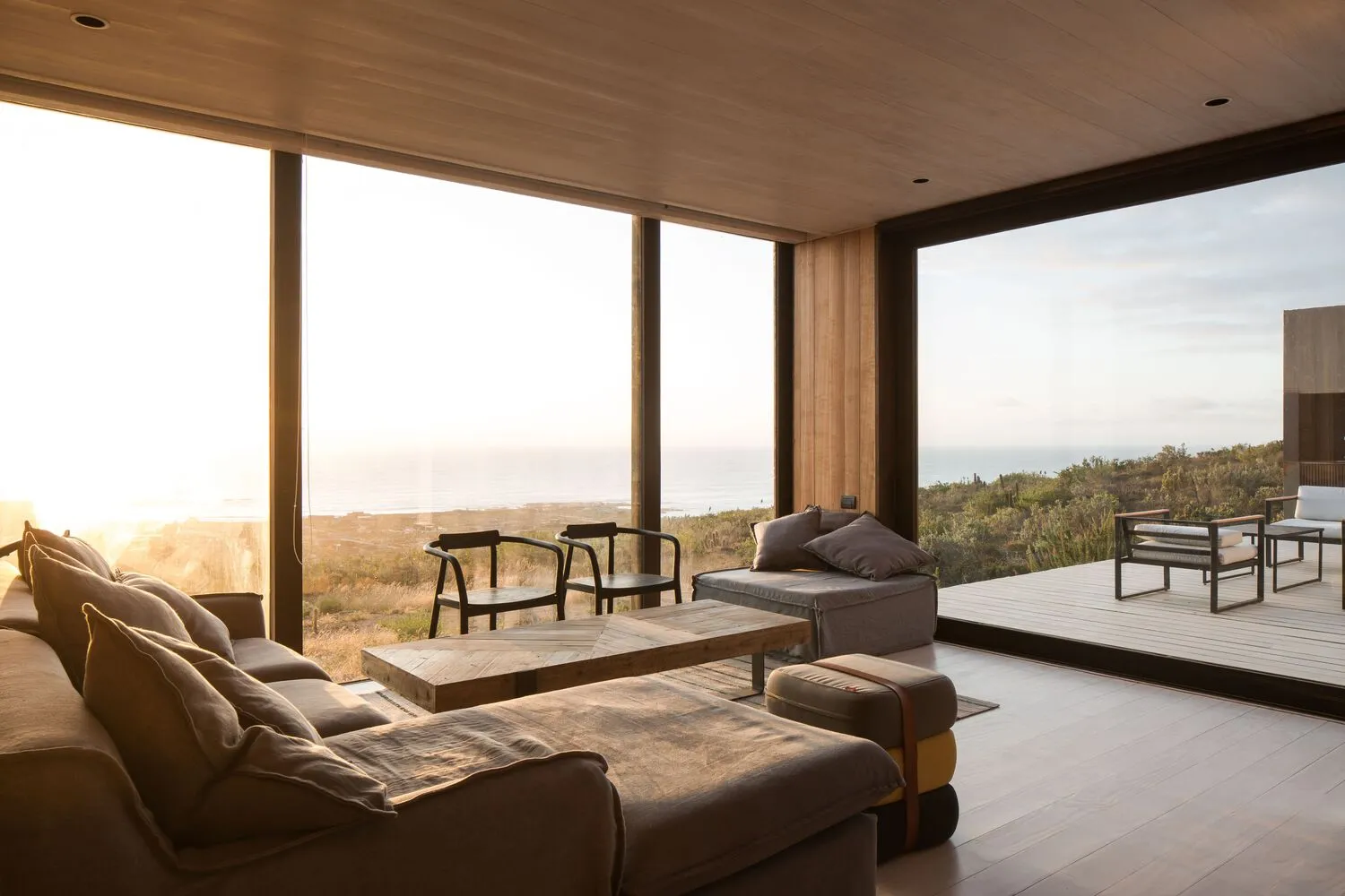 A luxurious coastal living room featuring wooden furniture, large windows overlooking the ocean, and a comfortable sectional