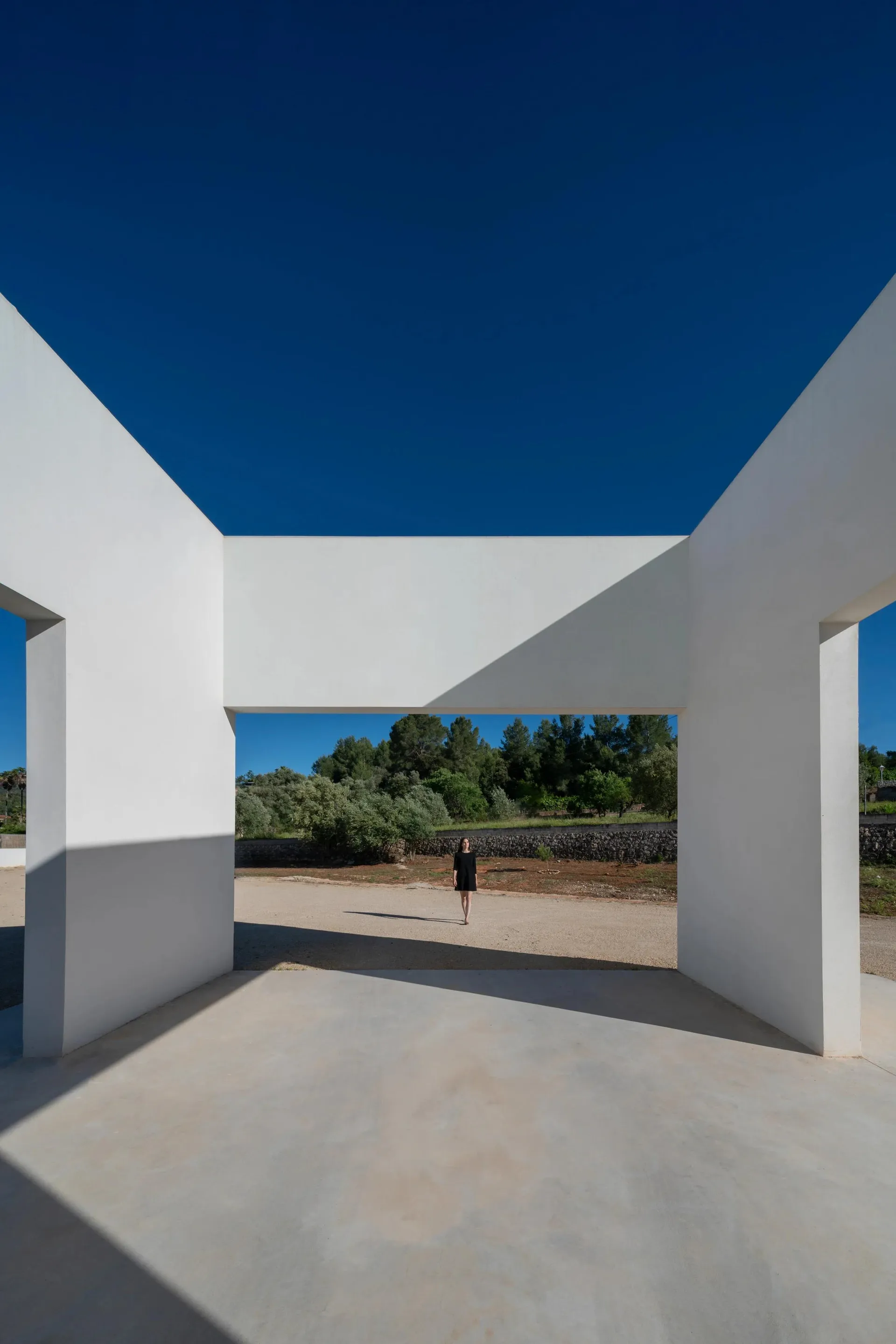 A minimalist concrete architectural space with a clear blue sky in the background.