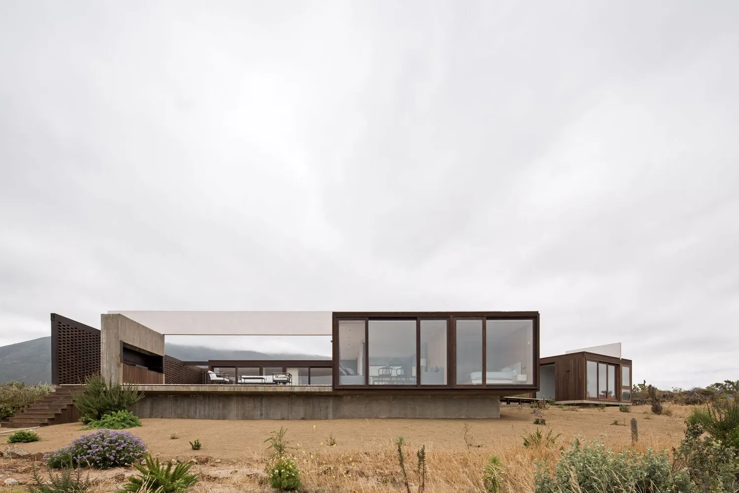A modern glass house with large windows and concrete foundation.