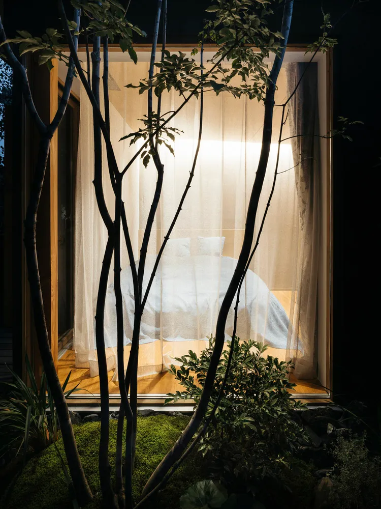 A serene minimalist bedroom with a bed covered in white bedding and a sheer curtain, surrounded by natural elements and soft