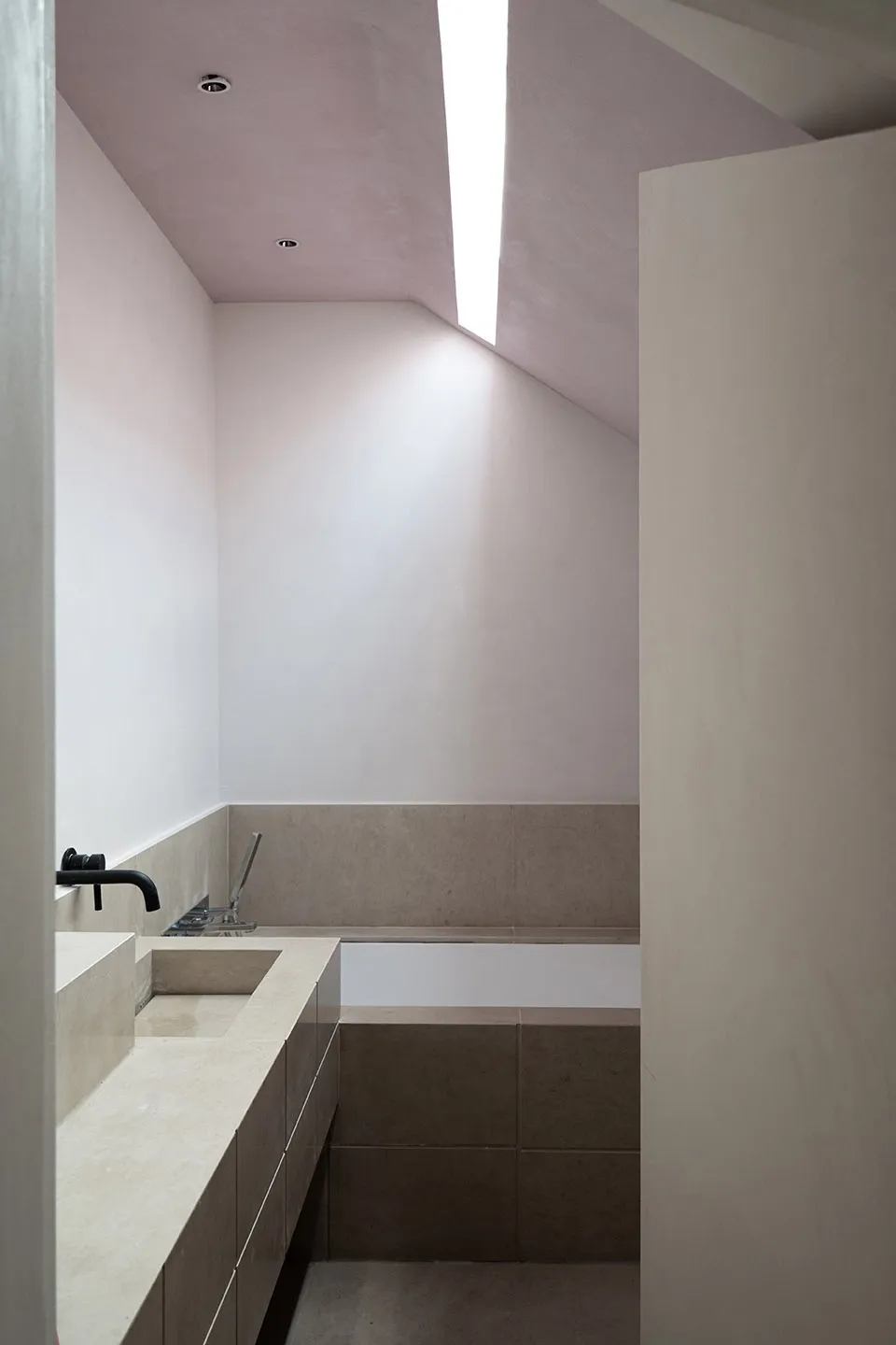 A modern minimalist bathroom with concrete walls and floor, featuring a sleek white bathtub and a built-in sink.