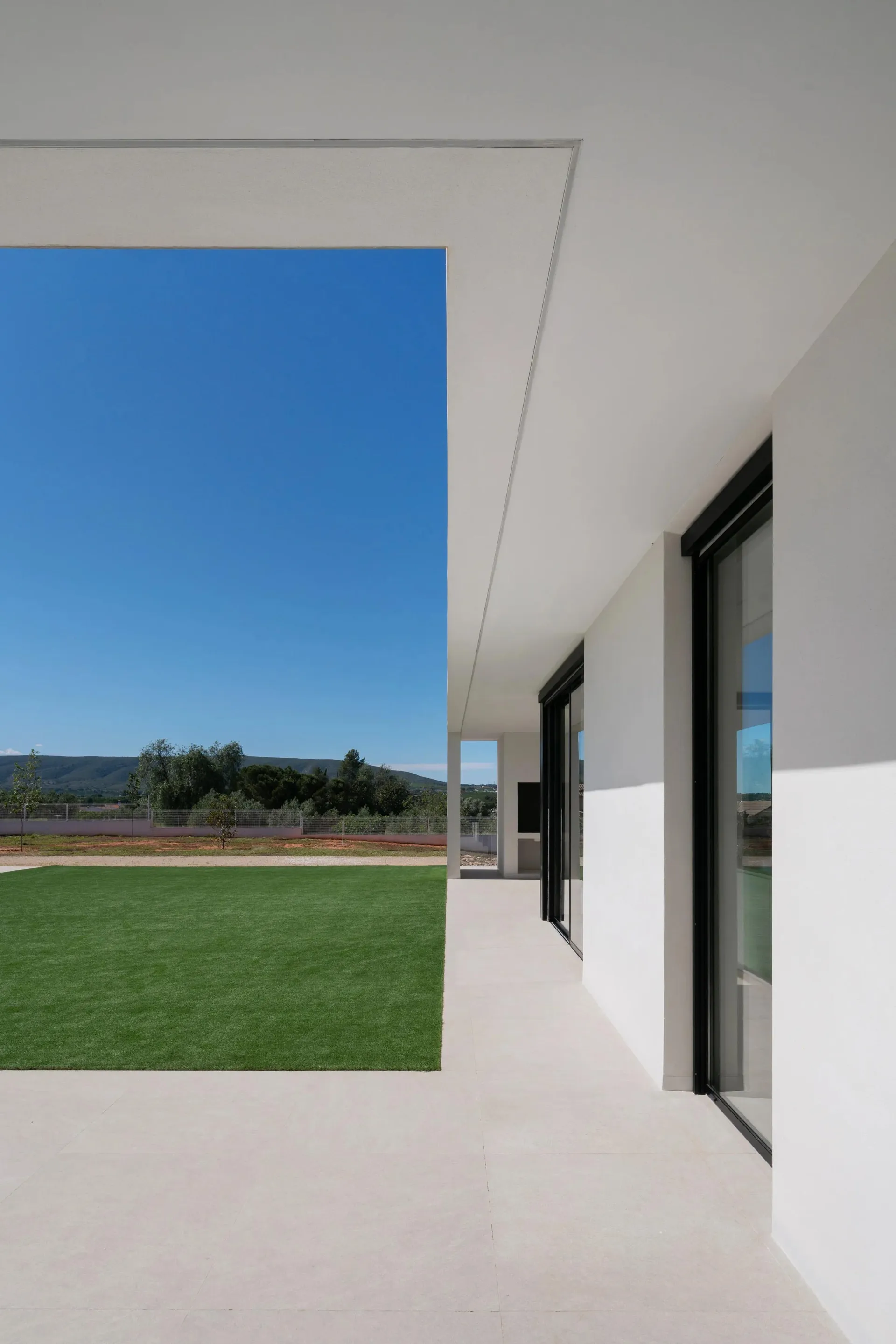 Modern minimalist house exterior with white walls and a green lawn.