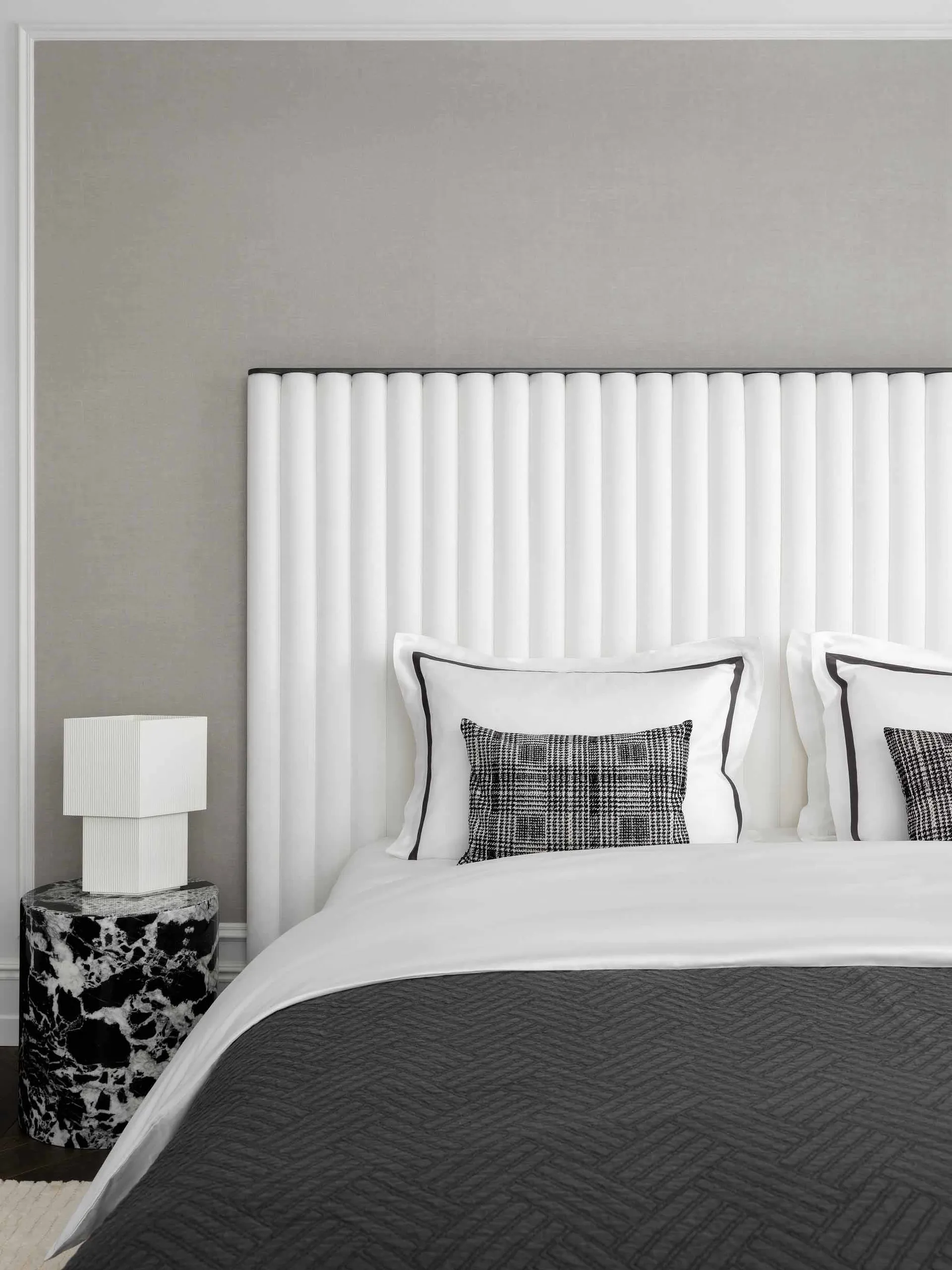 A minimalist bedroom featuring a white fabric headboard and a marble side table.