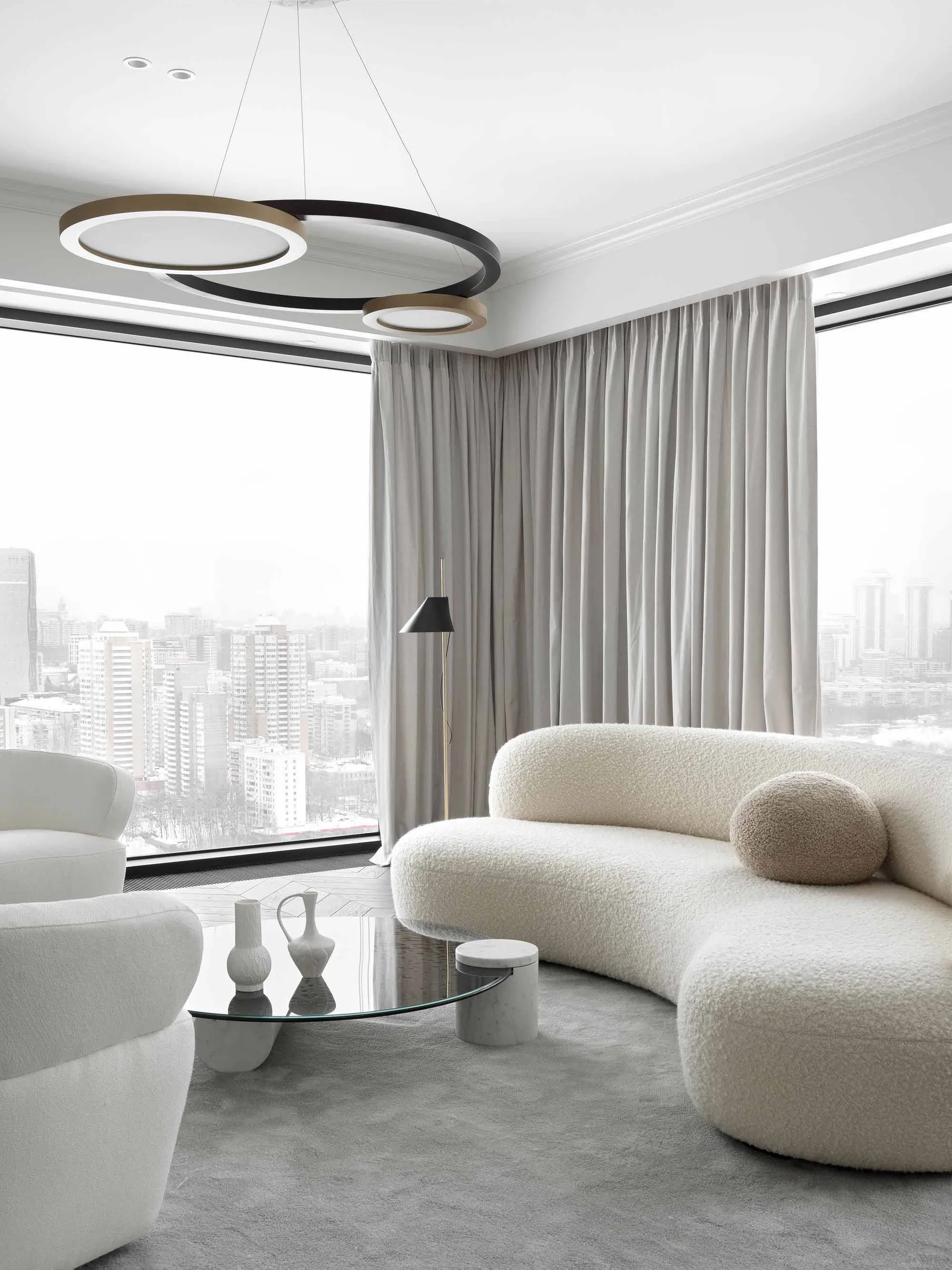 A modern white living room featuring a circular light fixture and curved sofa.