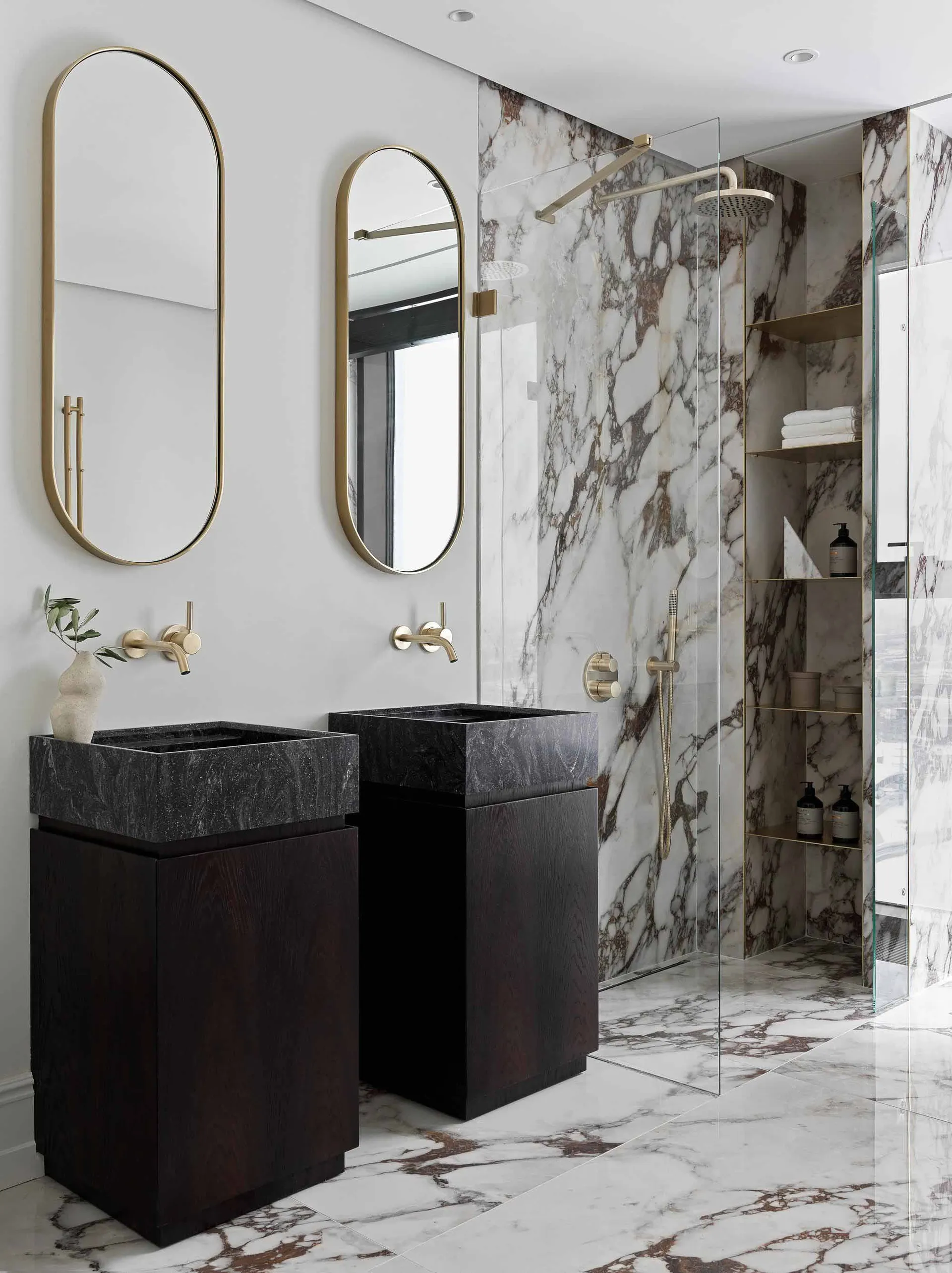 Modern bathroom with marble walls, brass fixtures, and wooden vanity