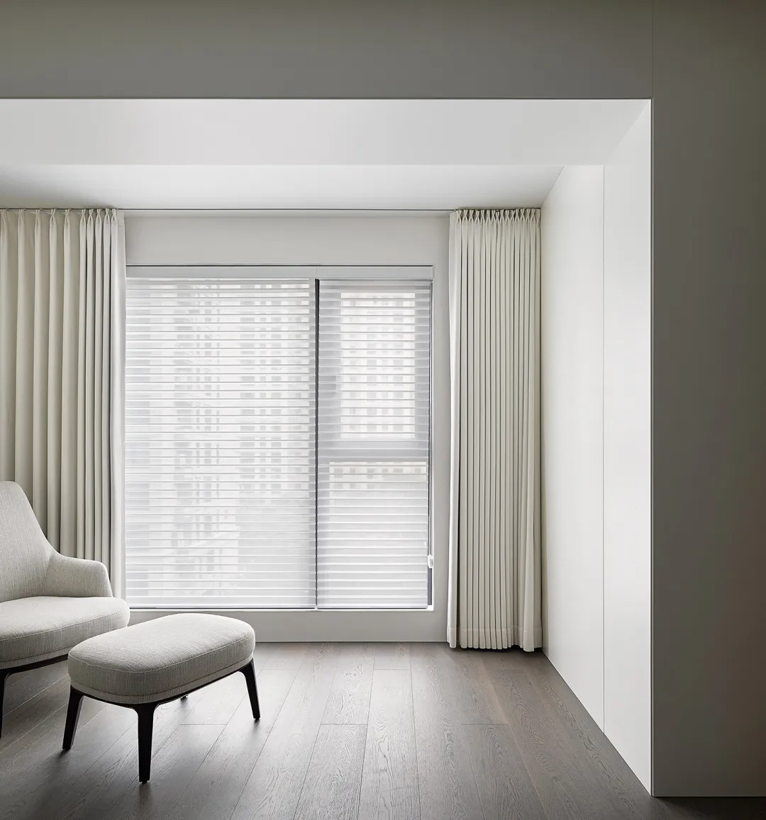 Modern neutral living room featuring a simple, minimalist design with light-colored furniture and wooden flooring.