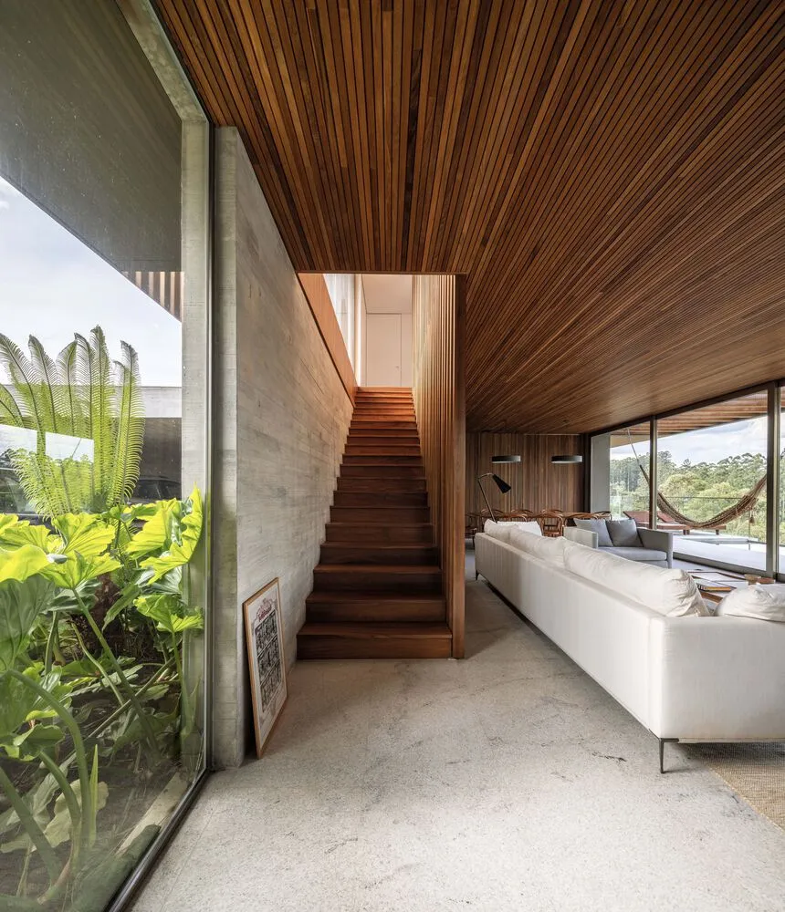 A modern living room featuring wooden elements and large windows with greenery outside.