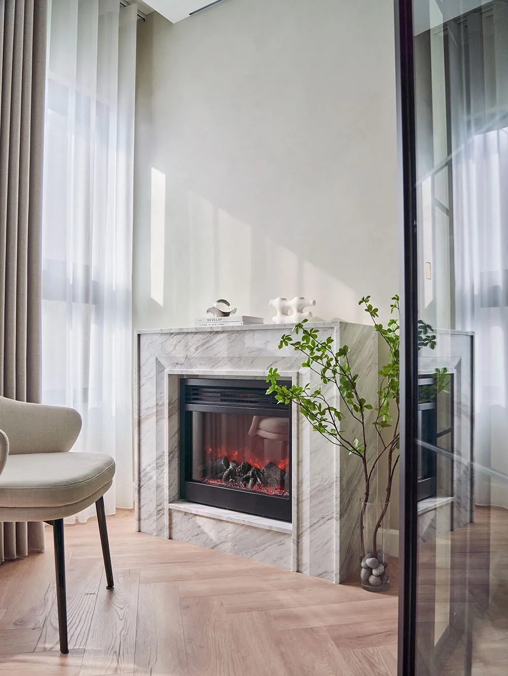 A modern living room with a marble fireplace, contemporary chair, and green plant.