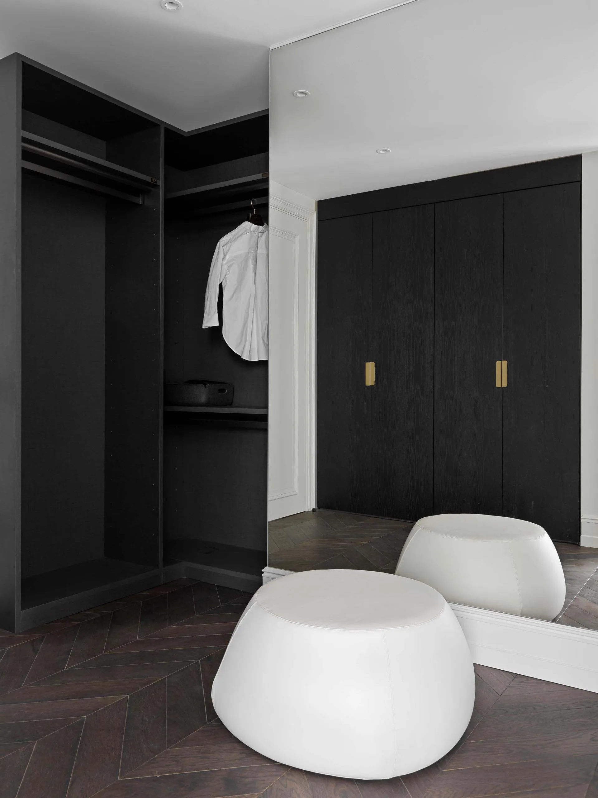 Modern minimalist closet with black wooden cabinets and white leather ottomans.