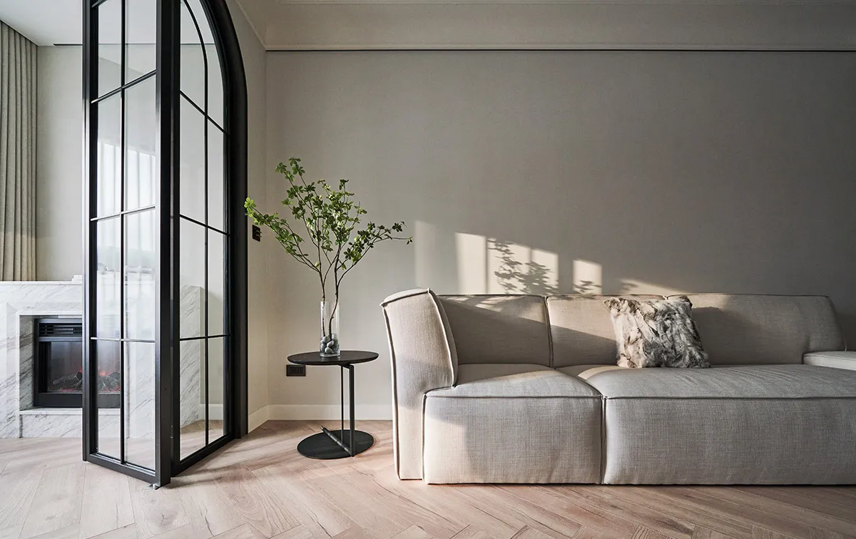 Modern minimalist living room featuring a light gray fabric couch with a small black side table holding a vase of greenery.