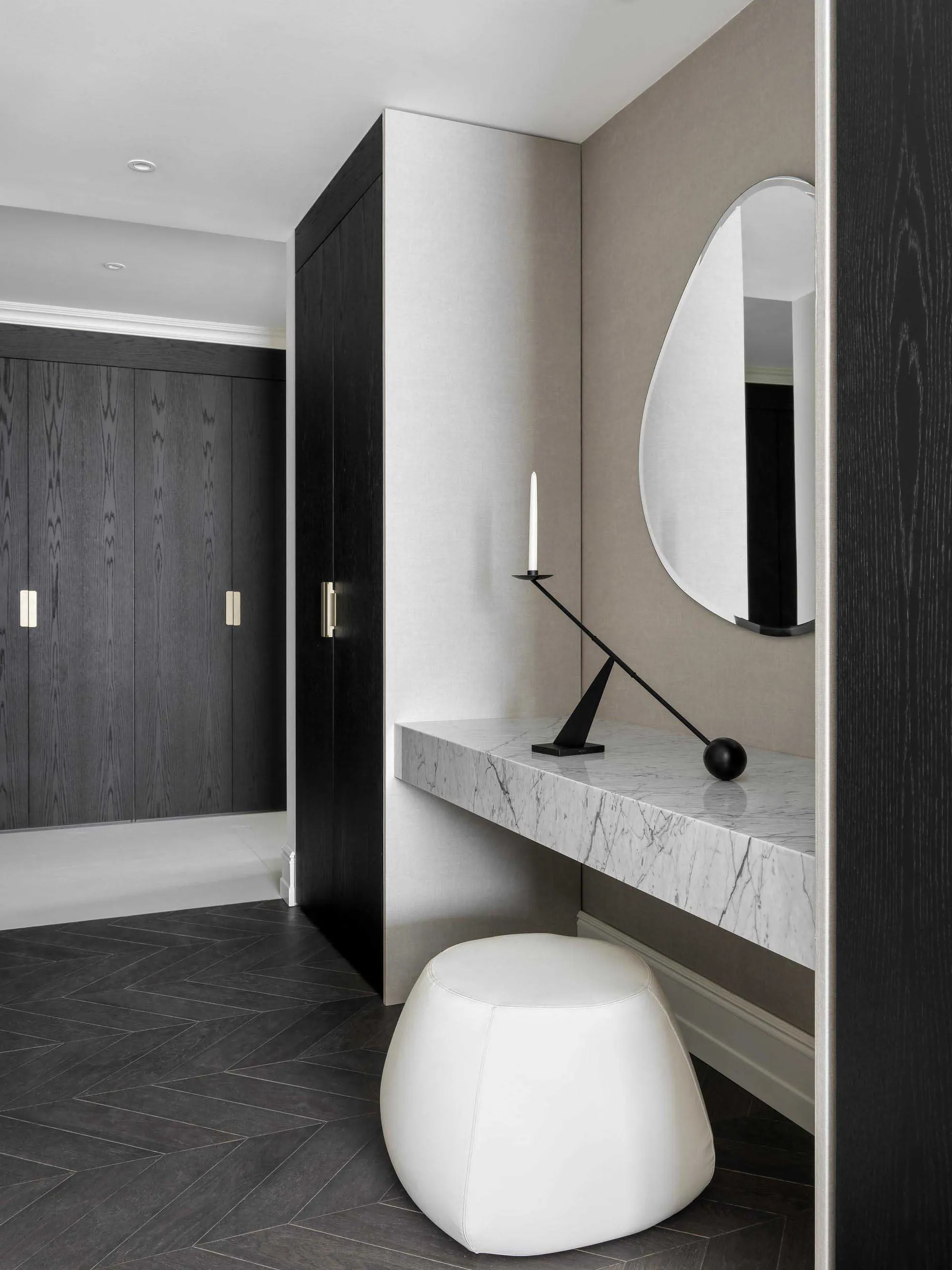 A modern vanity with marble countertop and white leather ottoman, featuring a minimalist design with a rounded mirror and bla