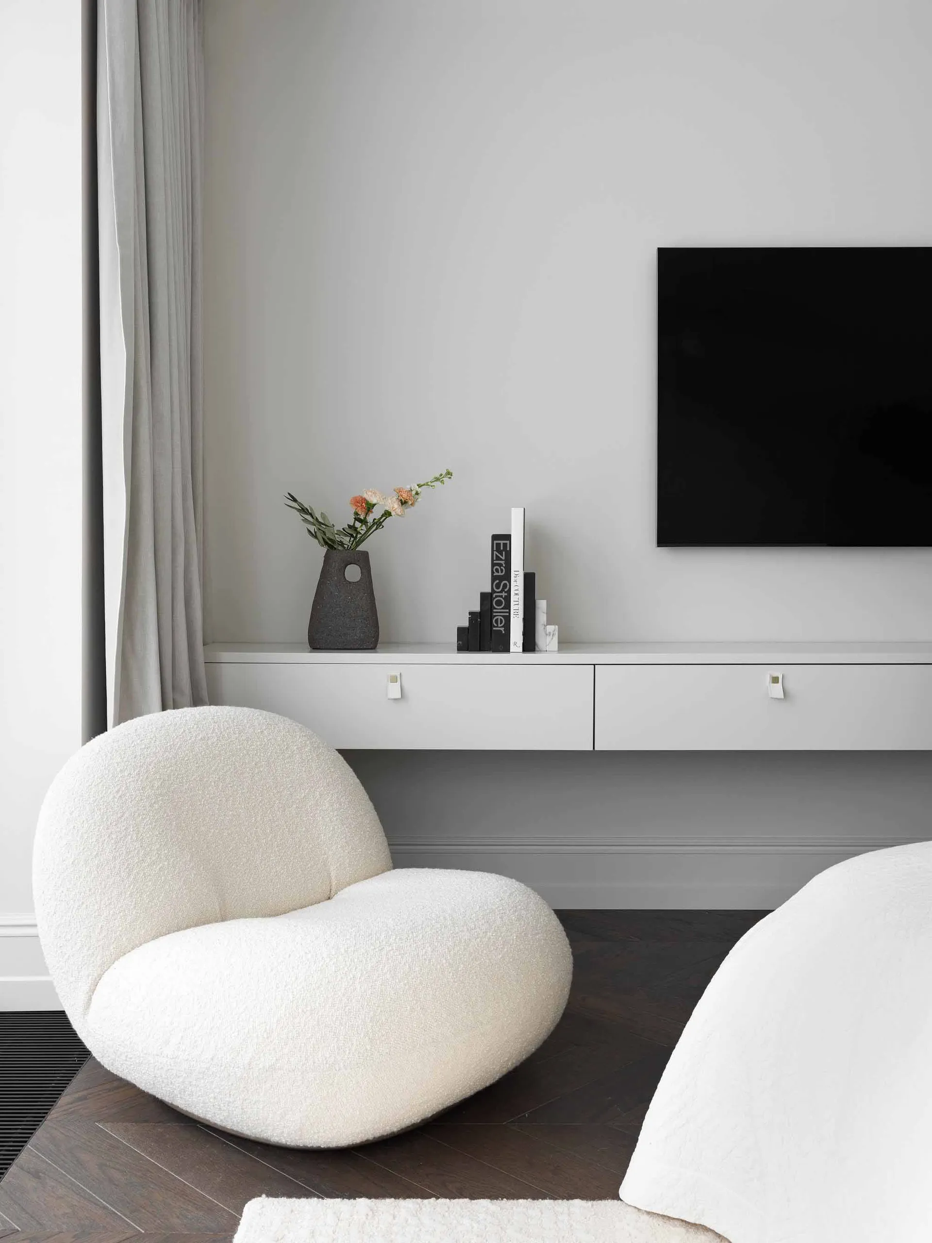 A modern white living room with a textured fabric chair, a shelf with a vase, and a television.