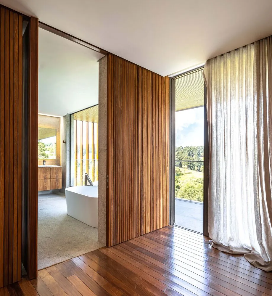 Modern bathroom featuring wooden paneling and a white stand-alone bathtub with a view of the outdoors through large windows.