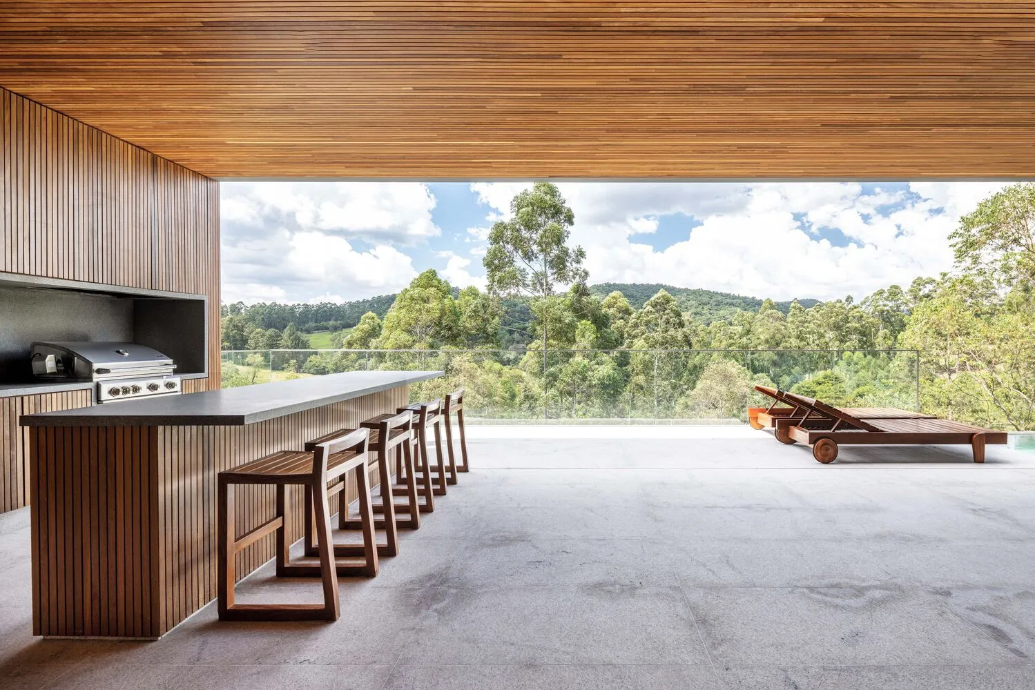 An outdoor kitchen with wood and concrete elements, featuring a large counter and seating area overlooking a scenic landscape