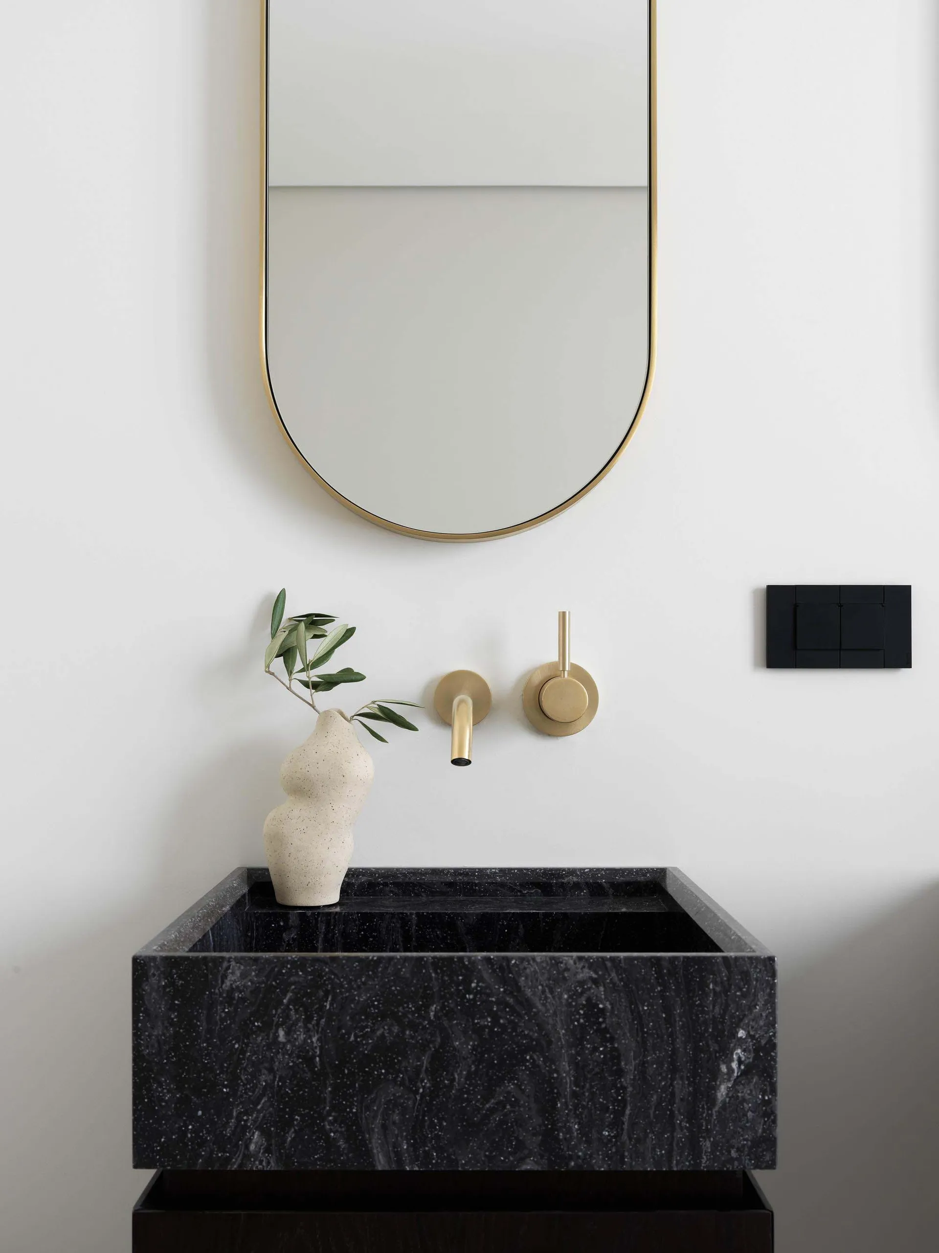 Modern bathroom with black marble sink, brass fixtures, and a minimalist design.