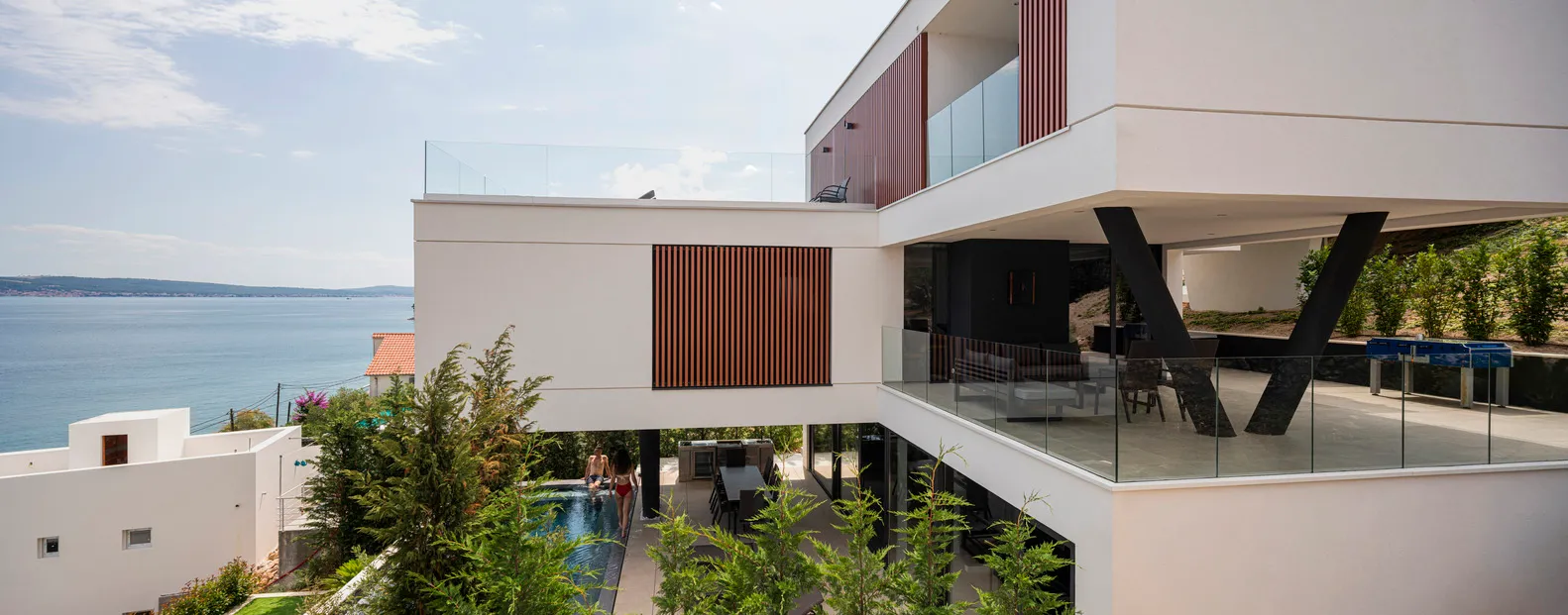 A modern residential exterior featuring glass walls and a swimming pool overlooking the sea.