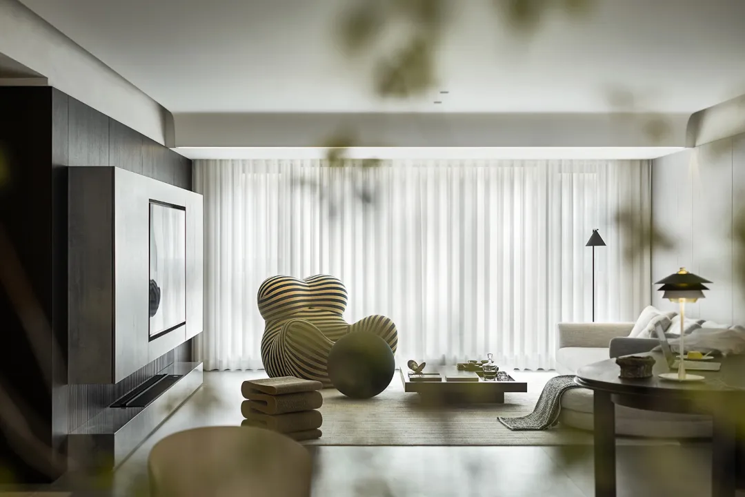 Modern minimalist living room with neutral tones, featuring a cozy armchair, low coffee table, and a sleek entertainment unit