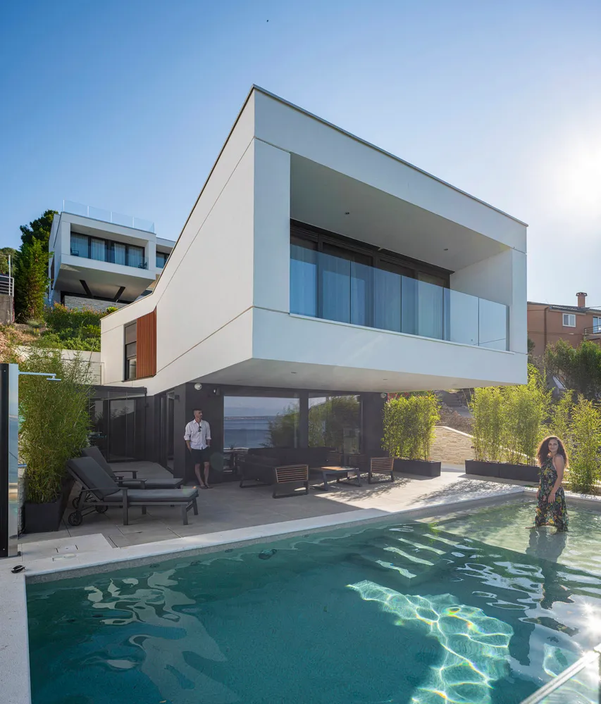 A modern residential exterior with glass walls and concrete surfaces.