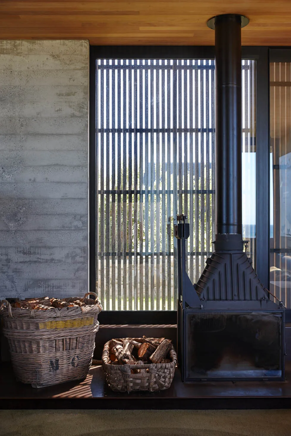 A modern industrial fireplace made of metal with a metal chimney and wood storage baskets.