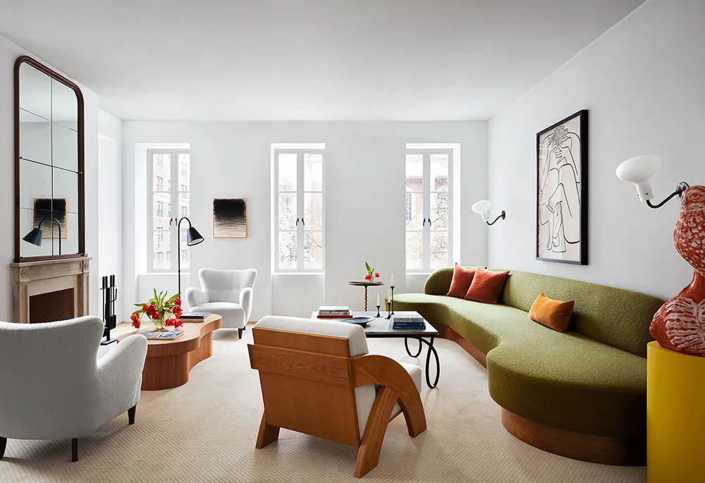 A modern living room featuring a green curved sofa, white armchairs, and a round coffee table with books and candles.