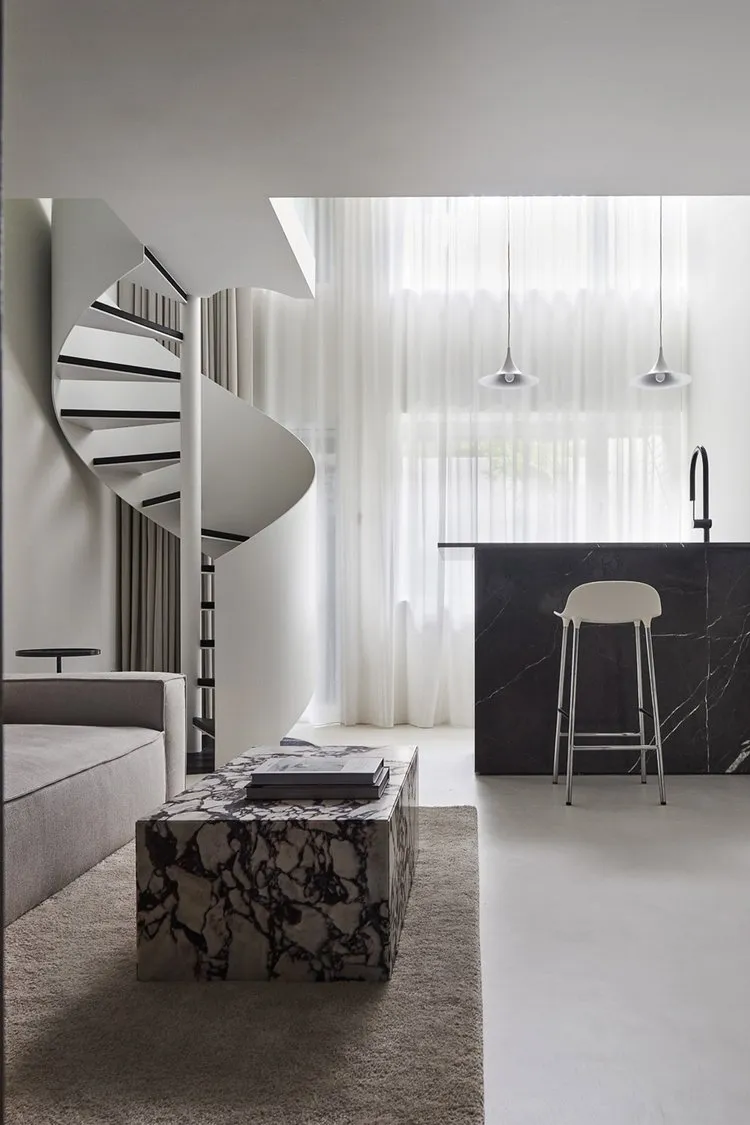 A modern living room featuring a spiral staircase, marble coffee table, and a sleek, minimalist design.