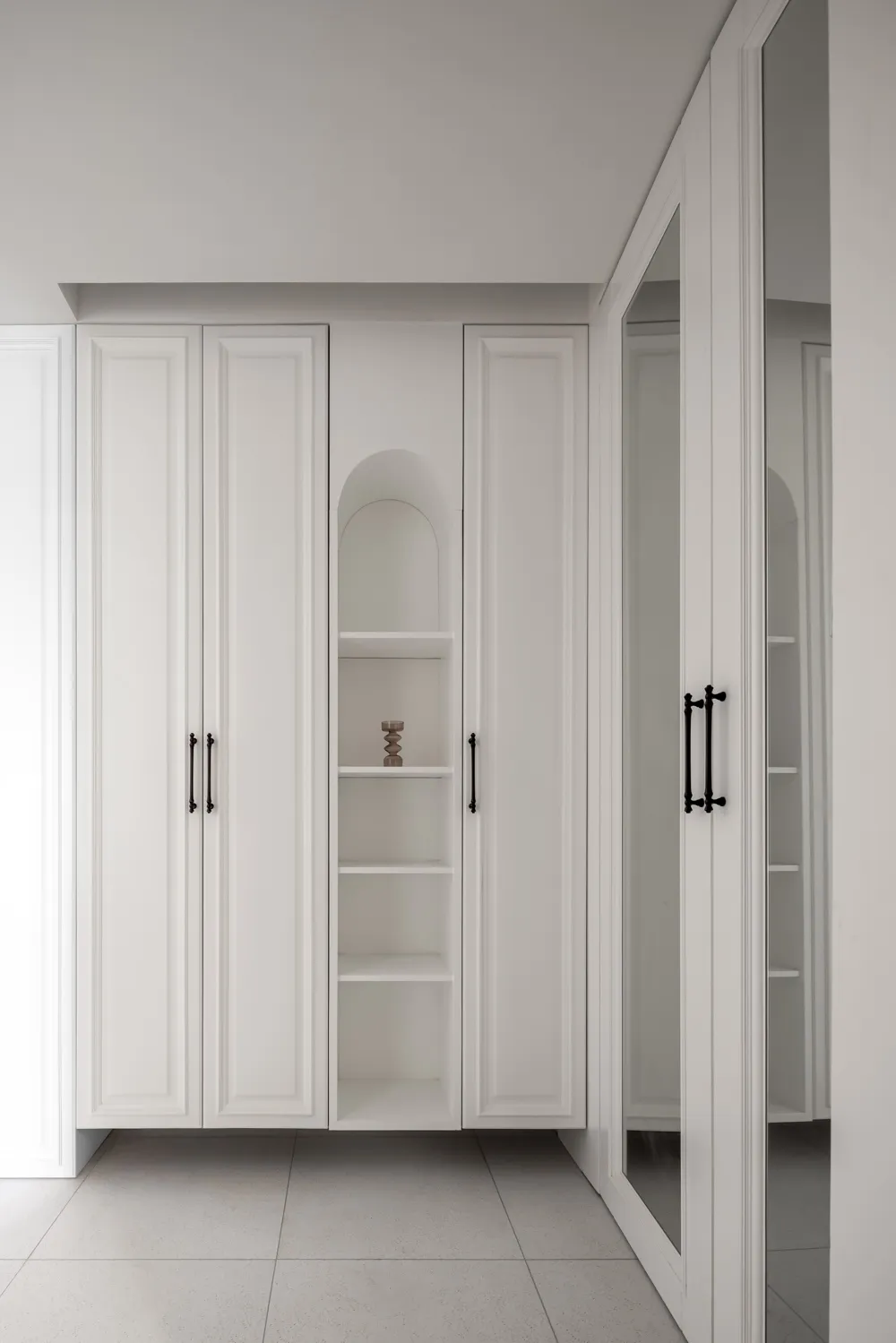 A minimalist white closet with sleek black handles and a small decorative object on the shelf