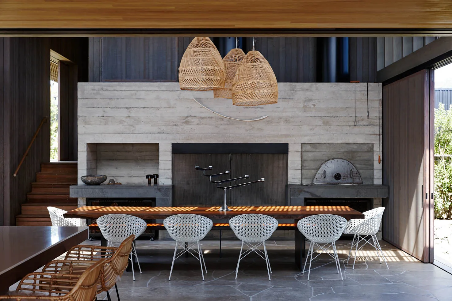 A modern living and dining room with concrete walls and a large table surrounded by white chairs.