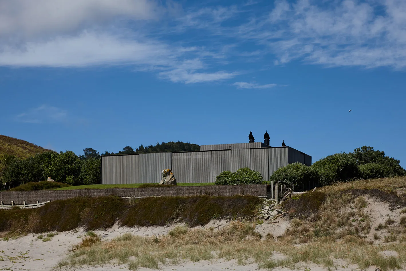 A modern metal-clad building exterior with a rectangular shape, standing on a grassy hillside with a blue sky in the backgrou