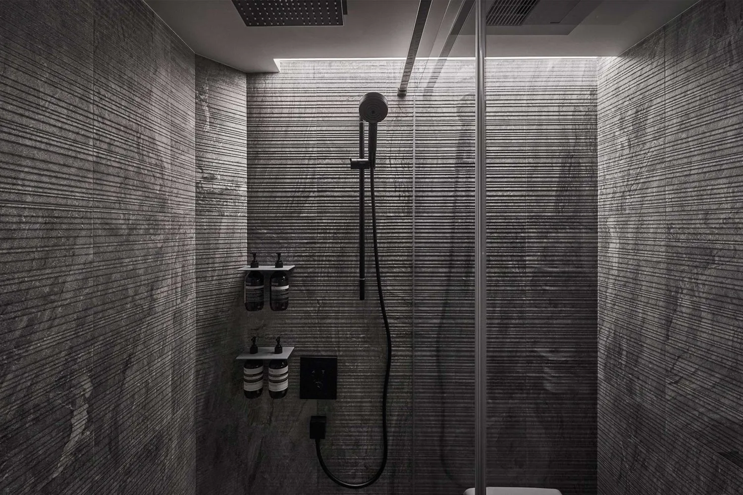 A modern minimalist bathroom with marble tiles, a glass shower enclosure, and sleek black fixtures.