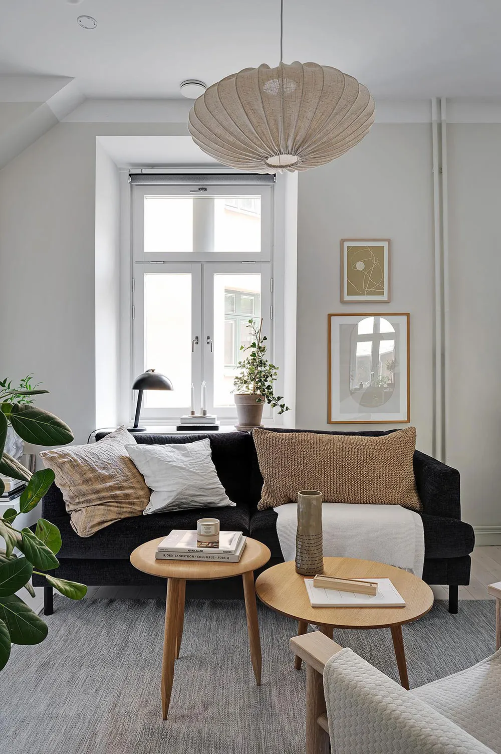 A minimalist living room with a black sofa, wooden side tables, and a modern pendant light.