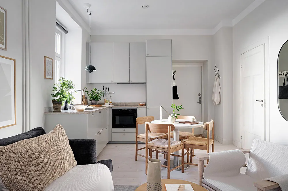Modern, minimalist kitchen with neutral-colored cabinets, black appliances, and light wooden furniture.