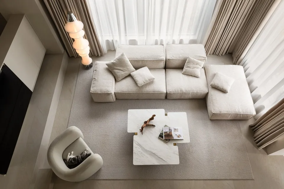 A stylish, minimalist living room with a white modular sofa, marble coffee table, and a cat lounging on a chair.