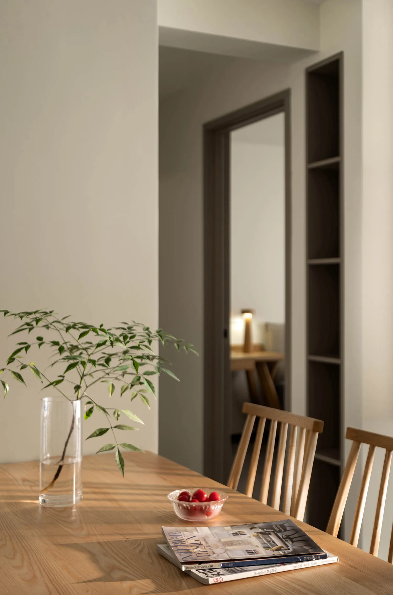 Modern dining room with wooden table, chairs, and a vase of greenery.